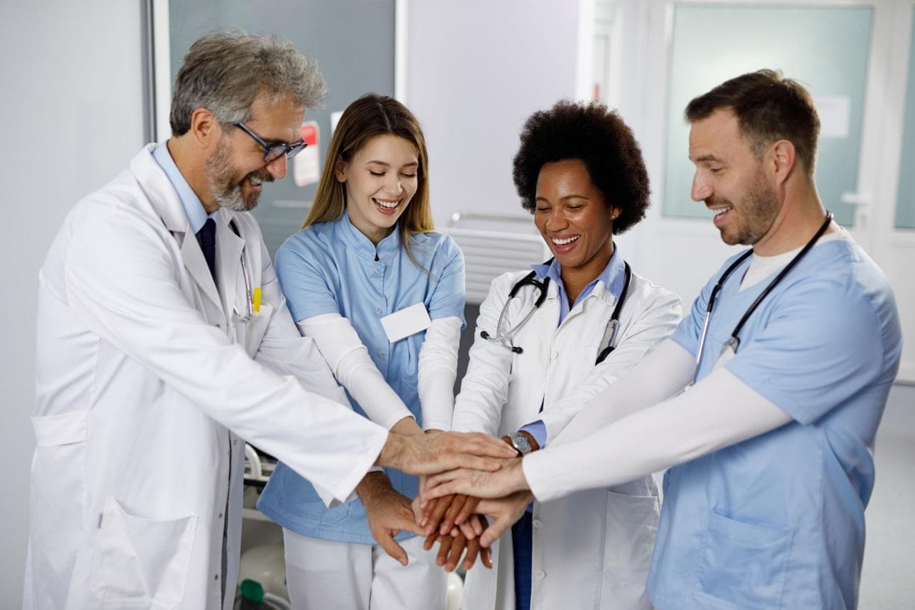 A team of healthcare professionals joining hands in a hospital corridor.