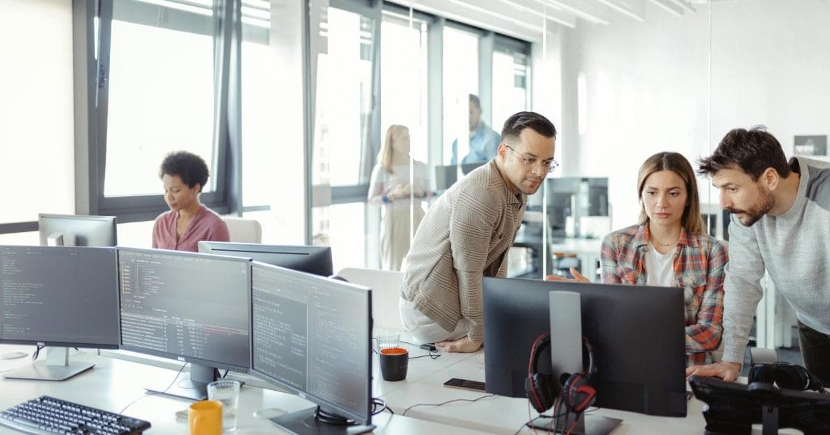 Software engineers collaborating around multiple monitors.
